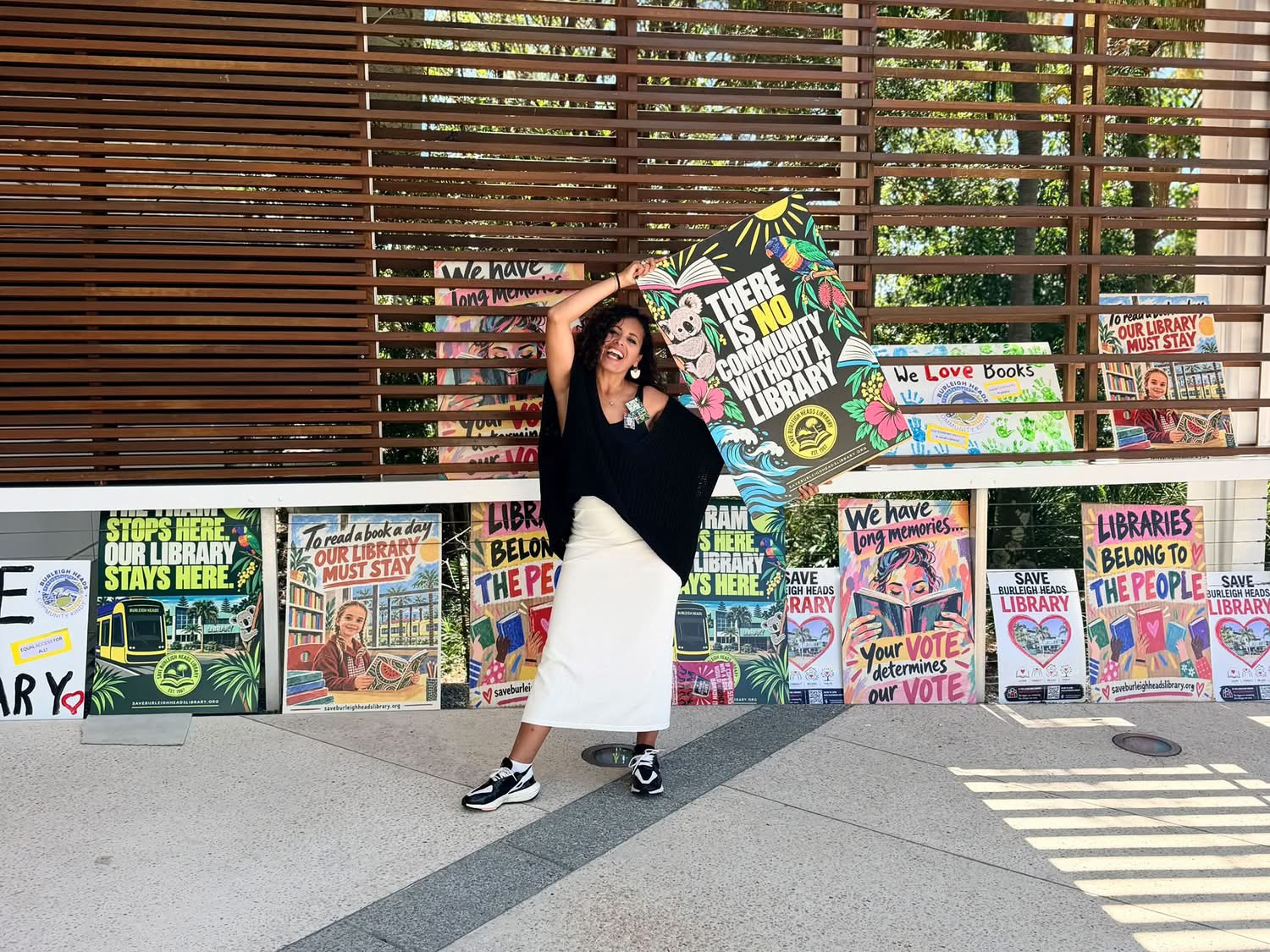 A campaigner celebrating, holding up a campaign poster reading 'There is no community without a library'